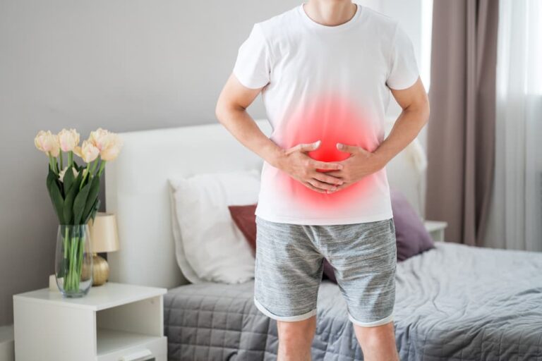 Homem segurando o abdômen com expressão de dor, indicando possível inflamação na região da vesícula biliar, sintoma comum da colecistite.